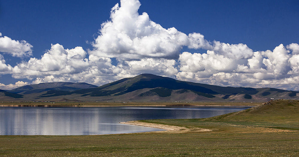 A still mountain lake reflecting summer clouds across the Mongolian steppe