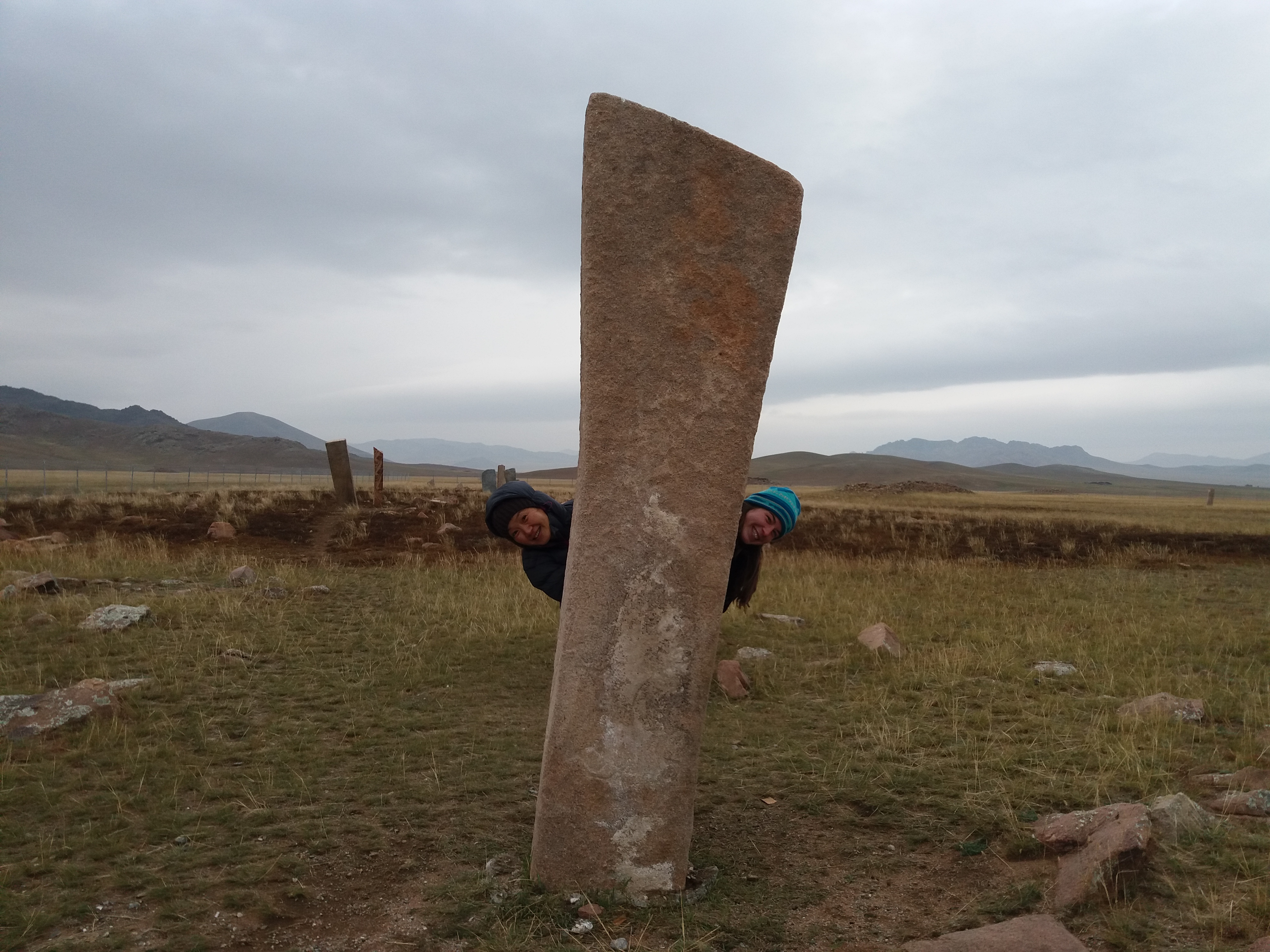 Travelers exploring ancient deer-stones on the Mongolian steppe under a moody sky